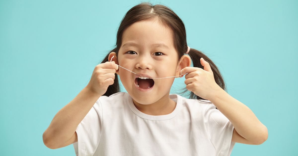 Young girl learning to floss her teeth