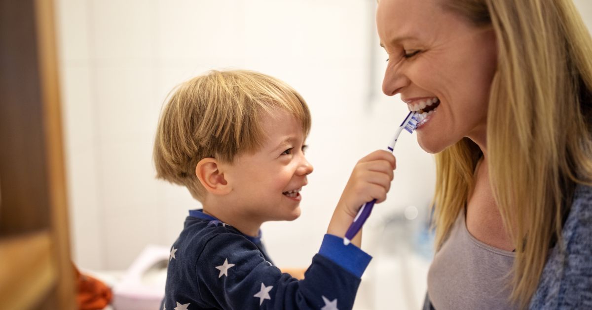 Child helping to brush their mother's teeth