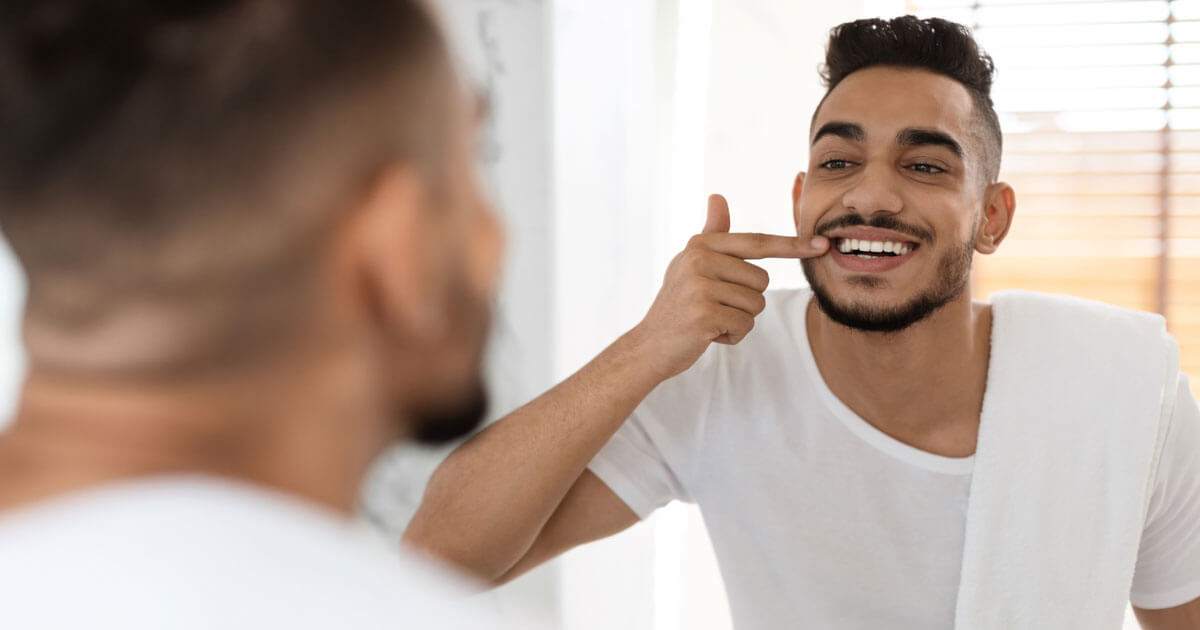 Man checking his teeth in a bathroom mirror