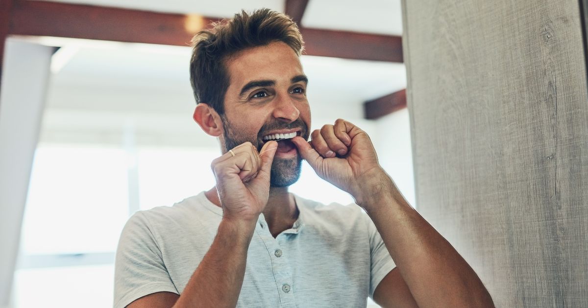 Man flossing his teeth in front of a mirror